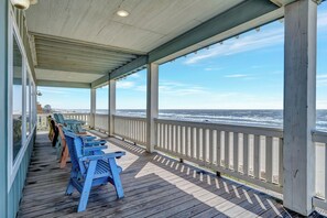 A covered deck with chairs and a view of the ocean.