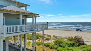 Une propriété située en bord de mer, dotée d’un balcon donnant sur l’océan, d’une plage de sable et offrant une vue sur un navire au loin.
