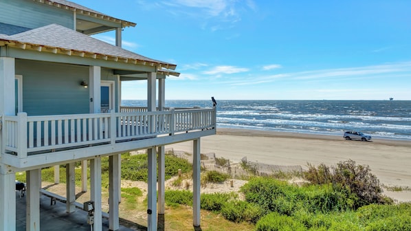 A beachfront property with a balcony overlooking the ocean, a sandy beach, and a distant ship.