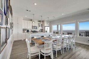 A spacious kitchen with white cabinetry, a central island, and a dining area with white chairs and a wooden table.