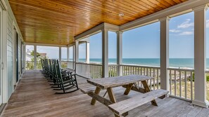 Une véranda couverte, dotée d’un plancher en bois et de bancs, qui offre une vue dégagée sur la plage et l’océan.