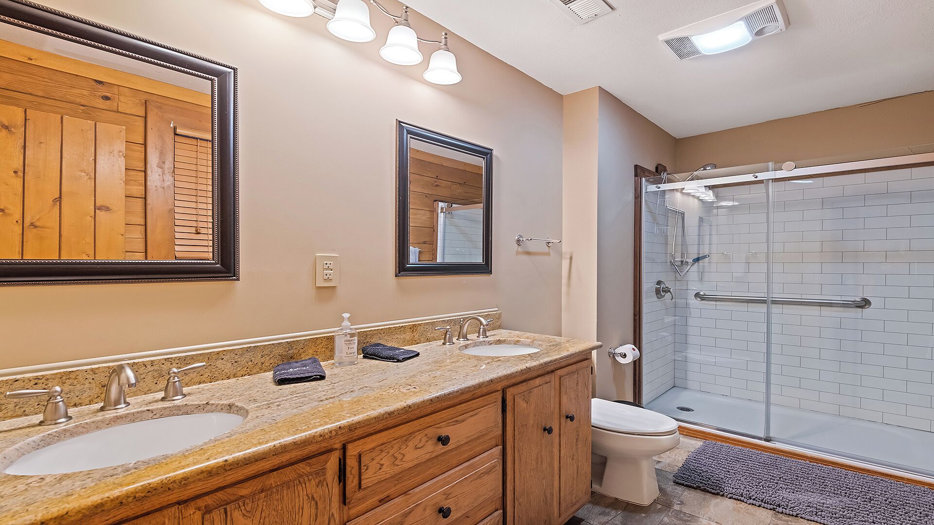 A bathroom with two sinks, a mirror, wooden cabinets, and a glass shower enclosure.