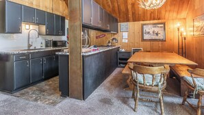 A rustic kitchen with dark cabinets, a marble countertop, and a wooden dining area with a table and chairs. - Chalet #12, Slope Side Ski in Ski Out Spacious Fam (Mammoth Lakes)