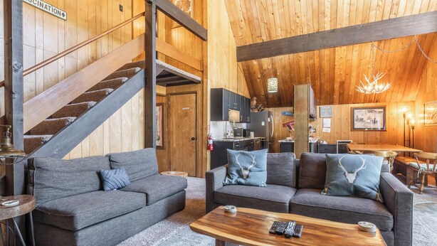 A cozy interior with two grey sofas, a wooden coffee table, and a staircase leading to a kitchen area. - Chalet #12, Slope Side Ski in Ski Out Spacious Fam (Mammoth Lakes)