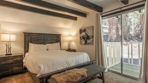 A bedroom with a large bed, two bedside tables, a bench, a painting, and a view of trees through a sliding glass door. - Chalet #12, Slope Side Ski in Ski Out Spacious Fam (Mammoth Lakes)