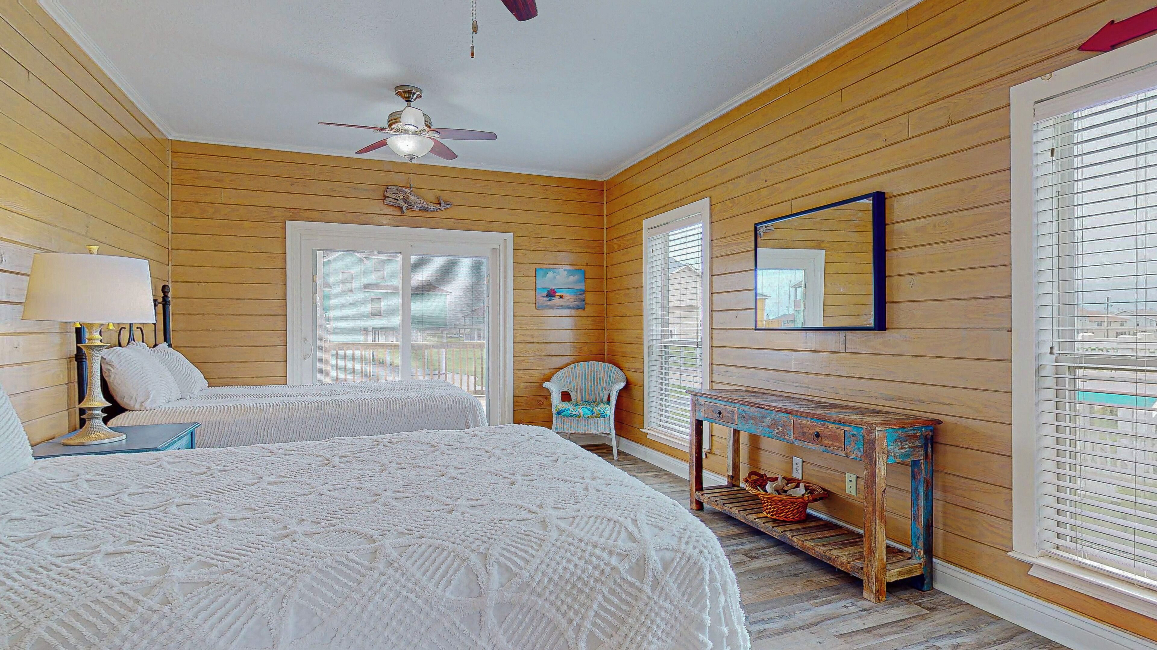 A bedroom with two beds, a ceiling fan, wooden walls, a window, and a small table.