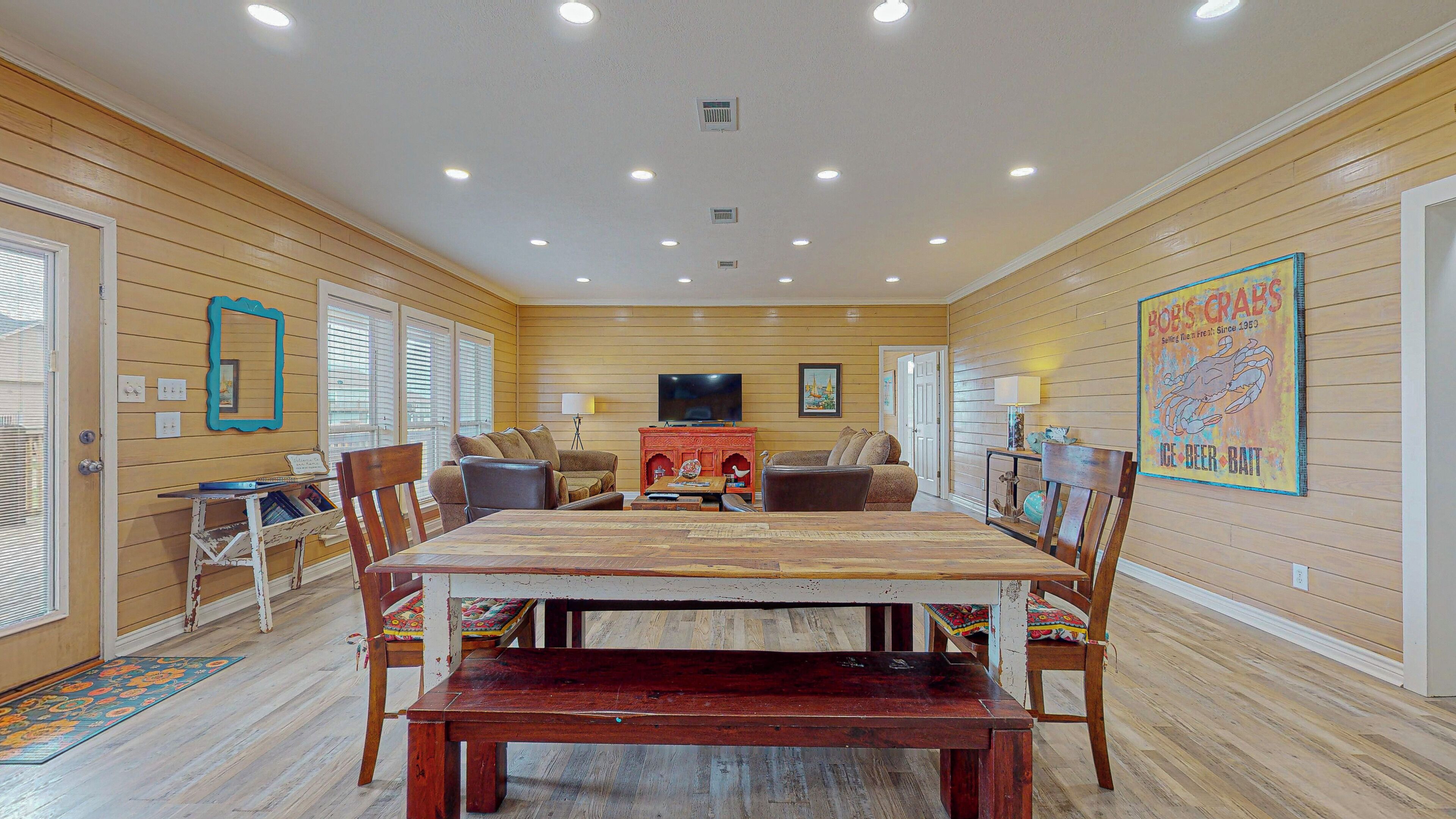 A spacious room with a wooden floor, a large dining table, and a television.