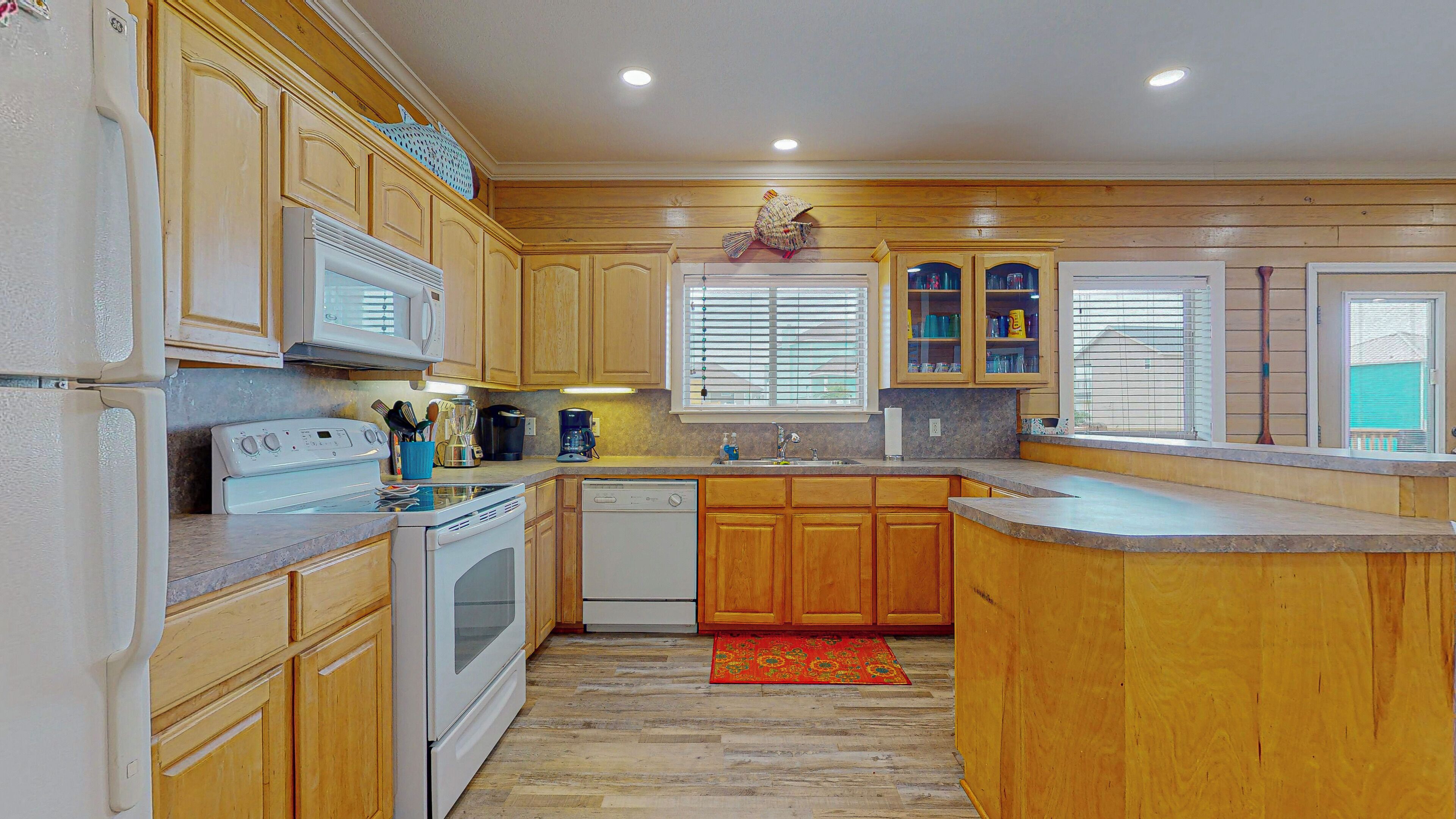 A kitchen with wooden cabinets, a microwave, stove, dishwasher, and a window with blinds.