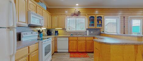 A kitchen with wooden cabinets, a microwave, stove, dishwasher, and a window with blinds.