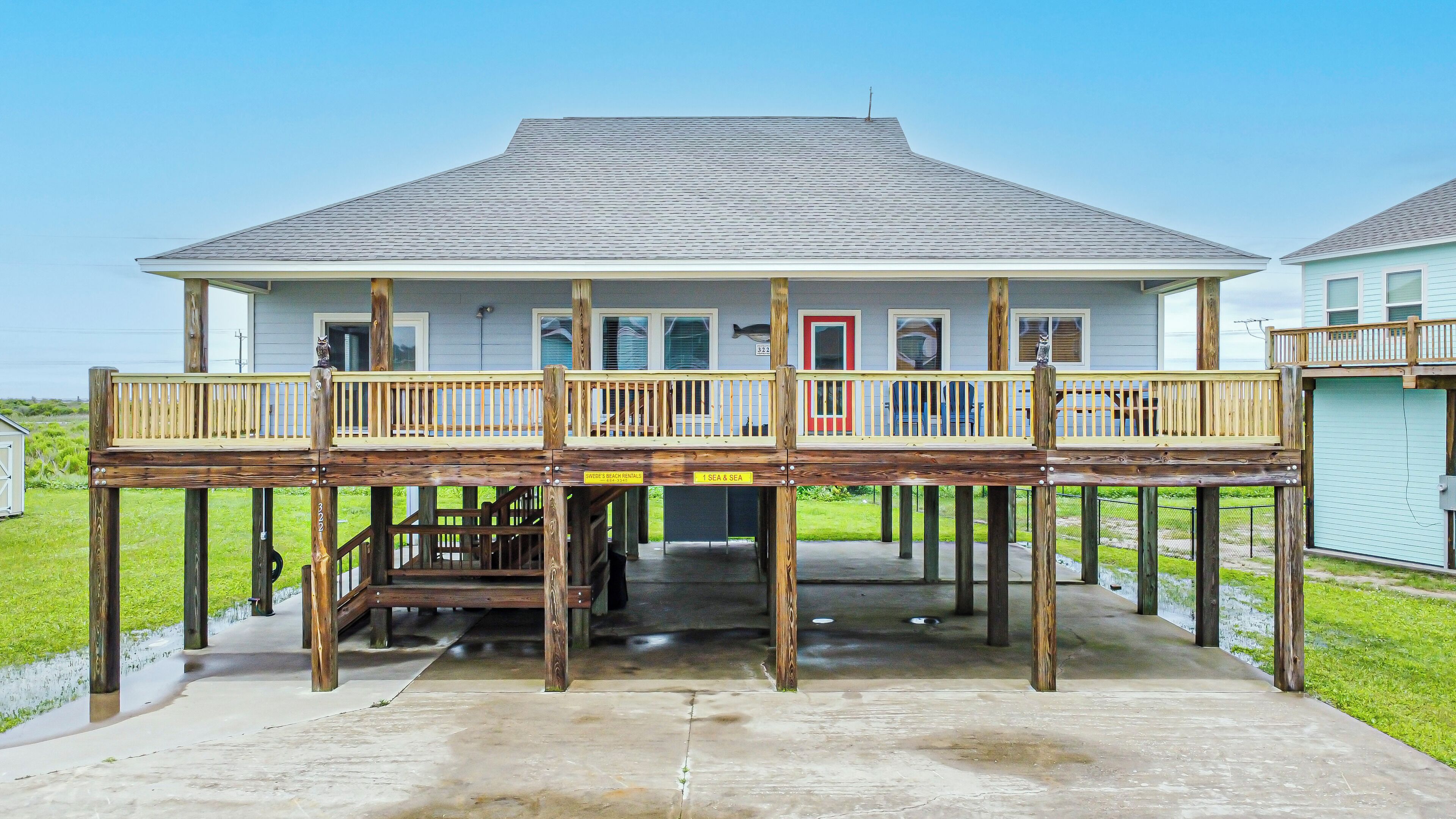Ein Strandhaus mit überdachter Terrasse, einer kleinen Treppe und einem einstöckigen Gebäude.