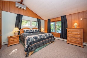 A bedroom with a bed, two bedside tables, a dresser, a window, and an air conditioning unit.
