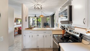 Une cuisine moderne avec des meubles blancs, une cuisinière noire et un luminaire suspendu.