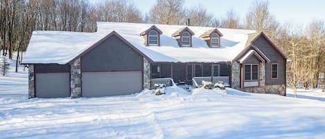 Une maison à deux étages avec une façade en pierre, plusieurs portes de garage et un toit recouvert de neige.
