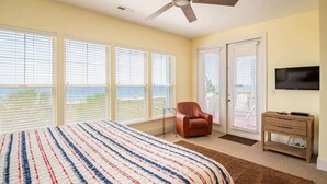 A bedroom with a large bed, a ceiling fan, a TV, and a view of the ocean through the windows. - Sandstep 616-2 (Carolina Beach)