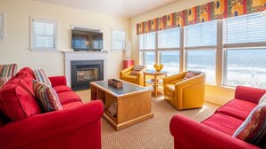 A living room with red sofas, a wooden coffee table, a fireplace, a television, and large windows with a view. - Sandstep 616-2 (Carolina Beach)