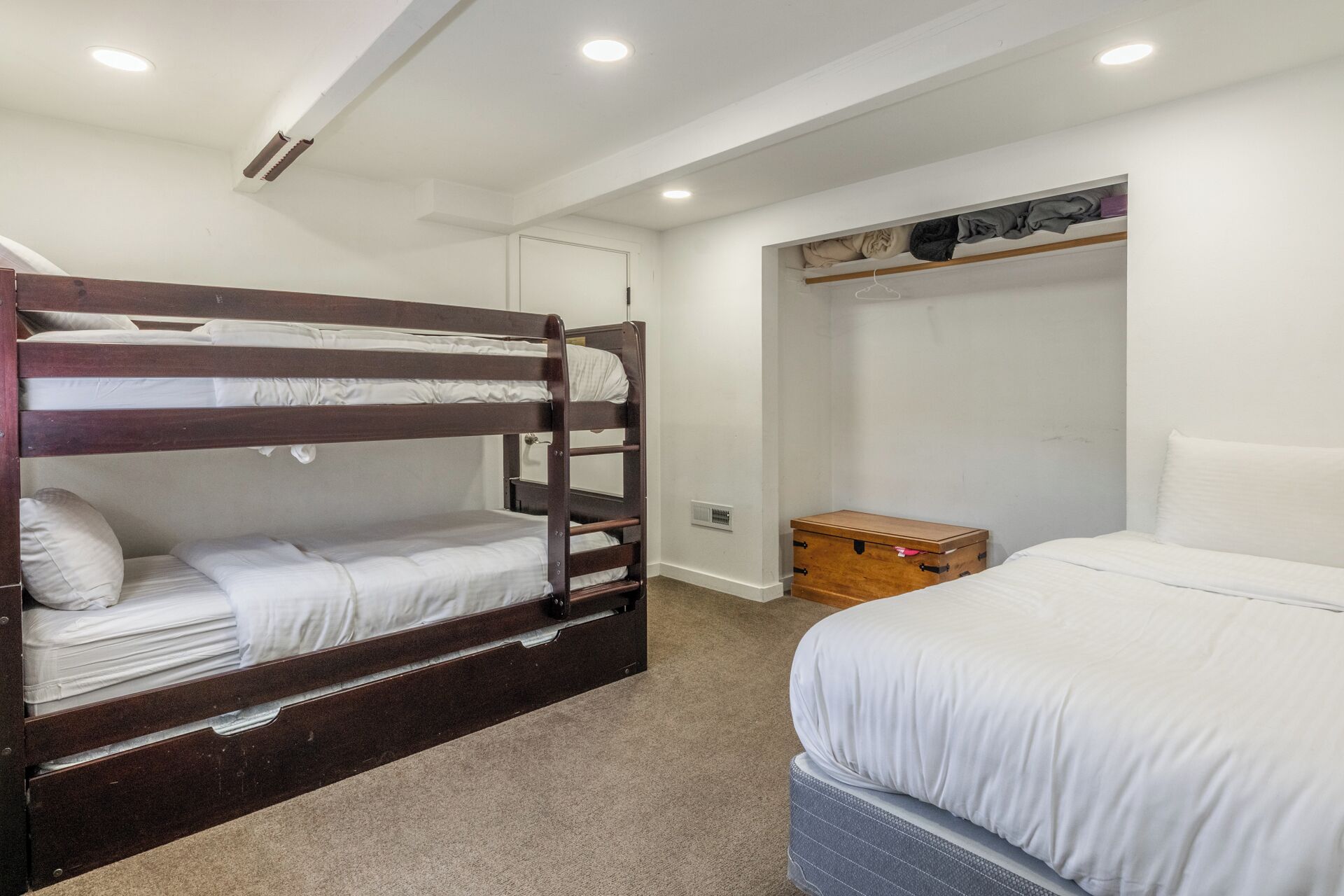 Une chambre avec un lit superposé en bois, un lit simple et une armoire.