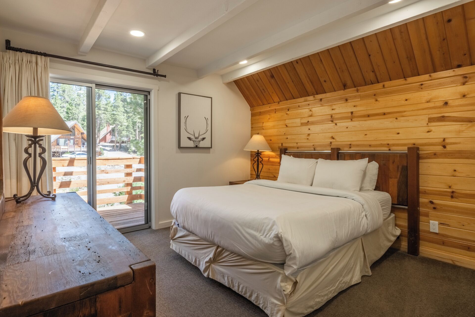 Een slaapkamer met een houten plafond, een bed met wit beddengoed, twee bedlampen en een raam met gordijnen.