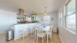 A modern kitchen with white cabinetry, a central island, and a dining area with white chairs. - Aloha Cabana: 2  BR, 1  BA House in Crystal Beach, Sleeps 8 (Crystal Beach)