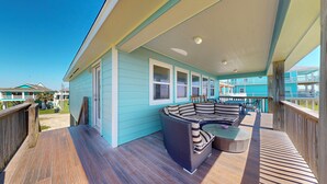 A covered deck with a wicker sofa and a glass table, wooden railings, and a view of other buildings. - Aloha Cabana: 2  BR, 1  BA House in Crystal Beach, Sleeps 8 (Crystal Beach)