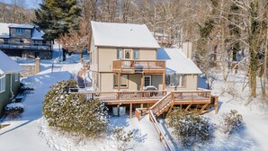 Una casa de dos pisos con balcón y terraza cubierta, rodeada de nieve y árboles.