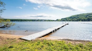 Un muelle se adentra en un lago tranquilo con cielo despejado y colinas distantes.