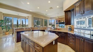 A modern kitchen with granite countertops, dark wood cabinets, and a large island. - FALL GETAWAYS 25% OFF Poolside Perfection 50ft Pool Dreamy Vibes (LA QUINTA)