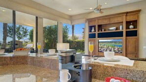 A modern kitchen with a Keurig coffee maker, a bowl of coffee pods, a glass of orange juice, and a view of a scenic landscape through large windows. - FALL GETAWAYS 25% OFF Poolside Perfection 50ft Pool Dreamy Vibes (LA QUINTA)