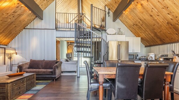 A spacious loft with a high ceiling, a central spiral staircase, a dining area with wooden chairs, and a kitchen with modern appliances. - Chalet #5, Ski In Ski Out Chalet at the Main Lodge (Mammoth Lakes)