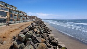 Ein Küstenhotel mit mehreren Balkonen mit Blick auf den Strand, einer steinernen Mole und freiem Blick auf den Ozean.