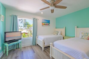 A bedroom with a television, two beds, a ceiling fan, and a window with curtains.