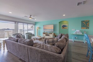 A living room with a large gray sofa, a TV, and a view of the ocean.