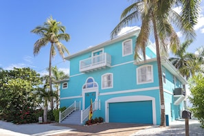 Uma casa de dois andares com fachada azul, detalhes brancos e varanda frontal, com uma bandeira.