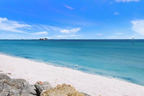 Una playa con aguas turquesas cristalinas, arena blanca y afloramientos rocosos.