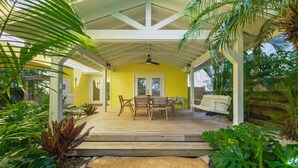 A covered outdoor area with a wooden deck, a table and chairs, and a bench. - A Time Out: *Quaint Cottage *Heated Pool *Across the street from the Bay! (Anna Maria)