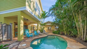 A pool area with a stone deck, lounge chairs, and a building with a porch. - A Time Out: *Quaint Cottage *Heated Pool *Across the street from the Bay! (Anna Maria)