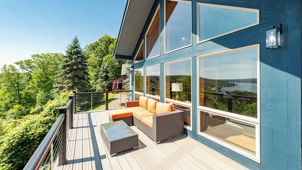 A modern house with a large deck, a sofa, and a glass wall offering a scenic view.