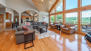 A spacious living area with a large sofa, a coffee table, and a fireplace. There are multiple windows offering a view of the outdoors.