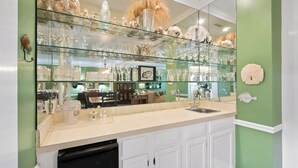 A kitchen with a glass display case filled with glassware and decorative items, white cabinetry, and a green accent wall. - Relax in this 3BR Villa with Pool Overlooking the 1st Fairway. (Georgetown)