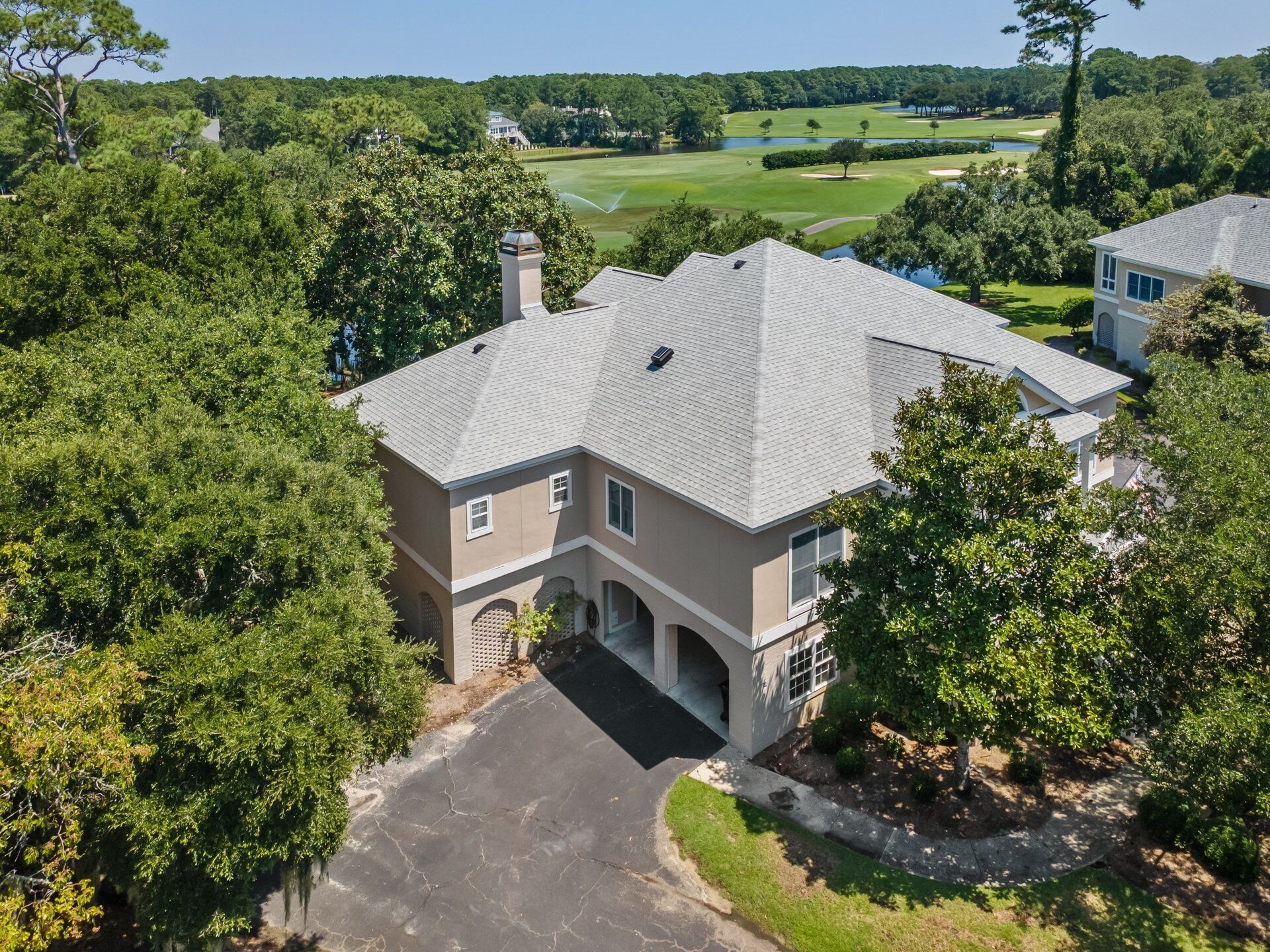 A large, single-story house with a sloped roof, surrounded by dense trees and a golf course in the background.