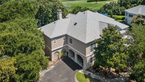 A large, single-story house with a sloped roof, surrounded by dense trees and a golf course in the background. - Relax in this 3BR Villa with Pool Overlooking the 1st Fairway. (Georgetown)