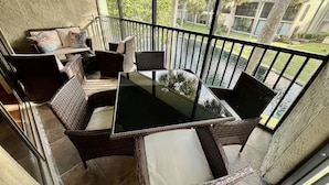 Ein Balkon mit Korbmöbeln, einem Glastisch und Blick auf einen Pool sowie Gebäude.