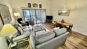 Ein Wohnzimmer mit Sofa, Couchtisch, Lampe und einem Essbereich mit Tisch und Stühlen.