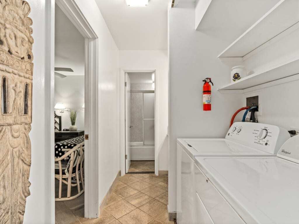 A laundry room with a Whirlpool washer and dryer, a fire extinguisher on the wall, and a doorway leading to a bathroom.