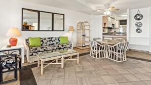 Un salon avec un canapé, une table basse et une table à manger avec des chaises. On aperçoit une cuisine au fond.