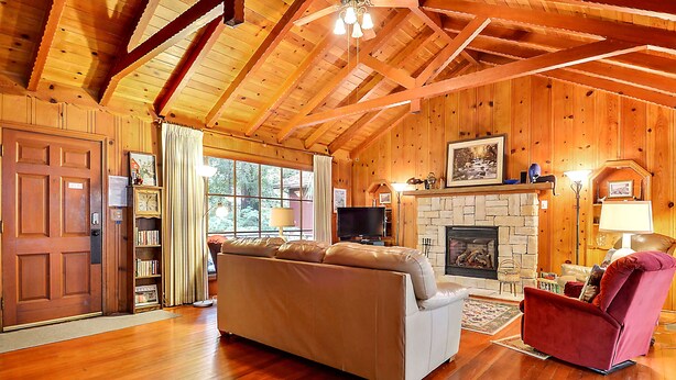 L’intérieur d’un chalet en bois, avec une cheminée, un canapé, un fauteuil rouge et un téléviseur.