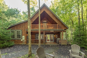 A cabin with a balcony, wooden exterior, and a gravel driveway.