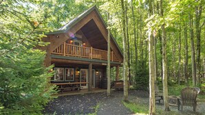 A cabin with a porch, wooden deck, and a fire pit.