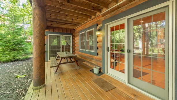 A log cabin with a wooden deck, a picnic table, and large sliding glass doors.