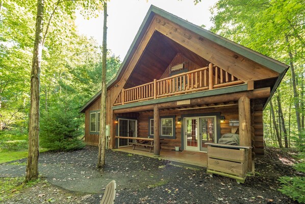 A log cabin with a balcony, wooden deck, and a welcoming entrance.