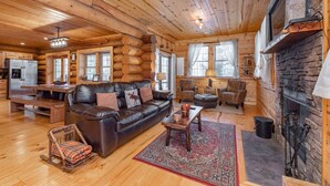 A log cabin interior with a leather sofa, a fireplace, and a dining area.